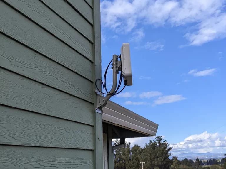 Subscriber CPE radio mounted on sage-green lap siding with a gutter leading to a wide Sonoma vista.